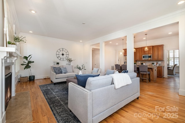 living area with light wood-type flooring, a fireplace with flush hearth, ornamental molding, and recessed lighting