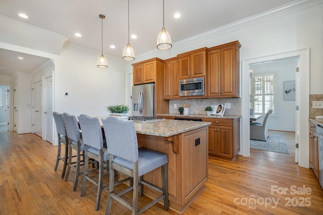 kitchen with a breakfast bar area, appliances with stainless steel finishes, light wood-type flooring, brown cabinets, and a center island