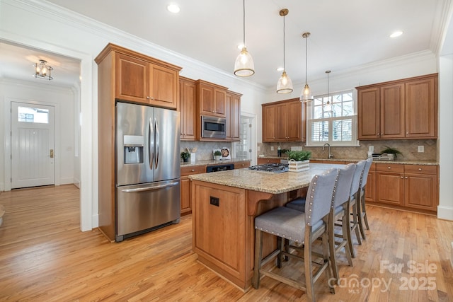 kitchen with brown cabinetry, light wood-style flooring, a center island, stainless steel appliances, and crown molding