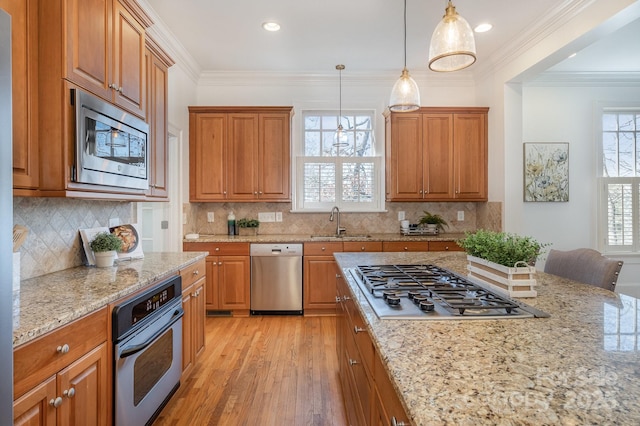 kitchen featuring a sink, appliances with stainless steel finishes, light stone countertops, brown cabinetry, and crown molding