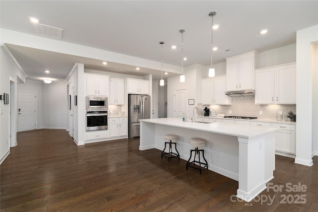 kitchen with under cabinet range hood, stainless steel appliances, a sink, visible vents, and decorative backsplash