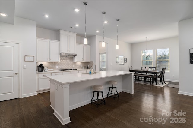 kitchen with white cabinets, dark wood finished floors, light countertops, under cabinet range hood, and gas stovetop