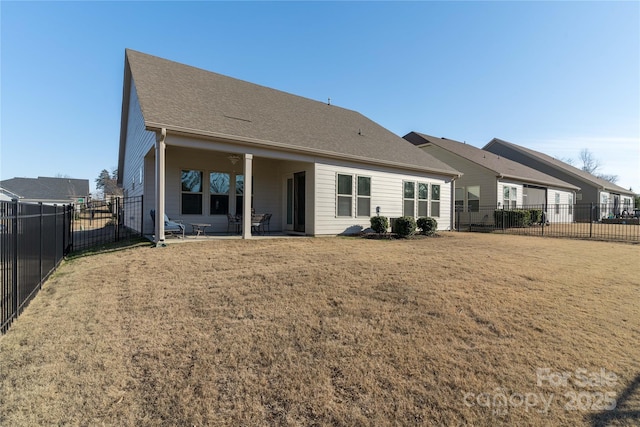 back of property with a patio area, a fenced backyard, a shingled roof, and a yard