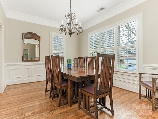 dining room with ornamental molding, light wood-type flooring, visible vents, and an inviting chandelier