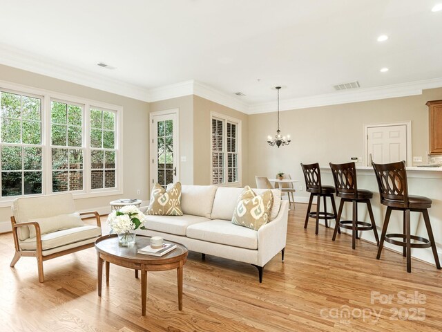 living room with ornamental molding, visible vents, a notable chandelier, and light wood-style flooring