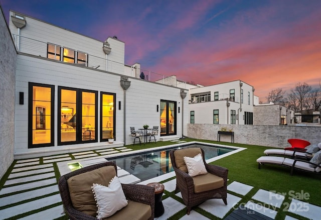 back of house at dusk with a fenced in pool, fence private yard, a lawn, and a patio