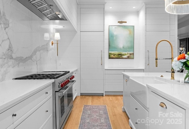 kitchen featuring light wood finished floors, light countertops, exhaust hood, white cabinets, and high end stainless steel range