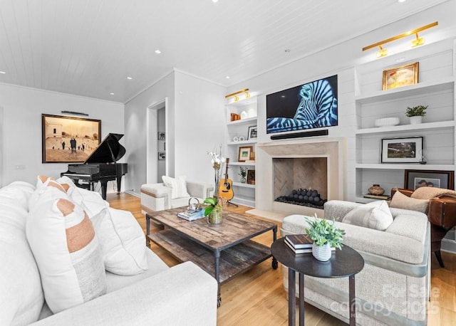 living room featuring built in features, light wood-style flooring, a fireplace, recessed lighting, and crown molding