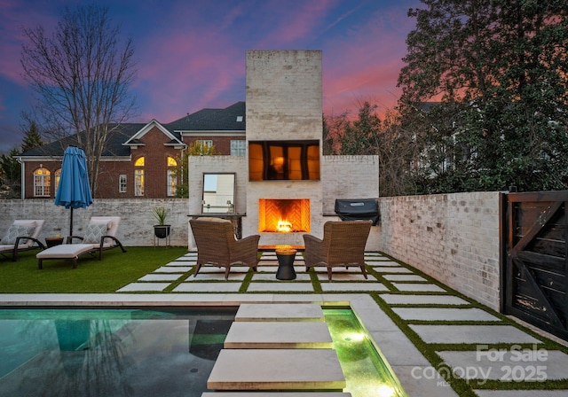 back of property with an outdoor pool, a patio, a warm lit fireplace, and a chimney