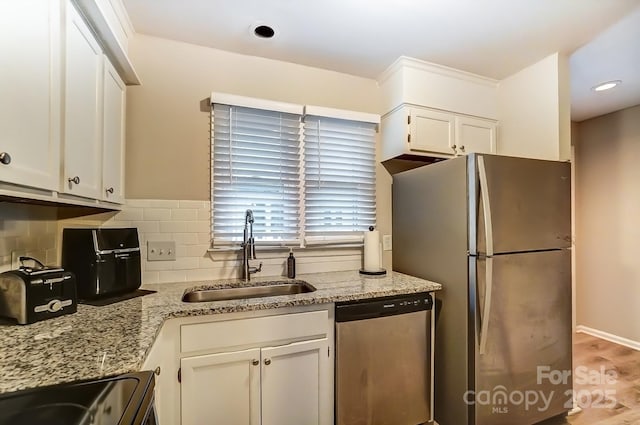 kitchen featuring light stone counters, a sink, stainless steel appliances, white cabinets, and backsplash