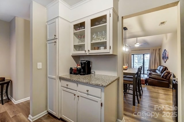 kitchen with visible vents, light stone counters, open floor plan, wood finished floors, and glass insert cabinets