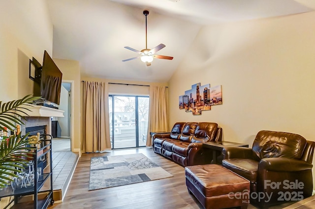 living area with a tile fireplace, high vaulted ceiling, a ceiling fan, and wood finished floors