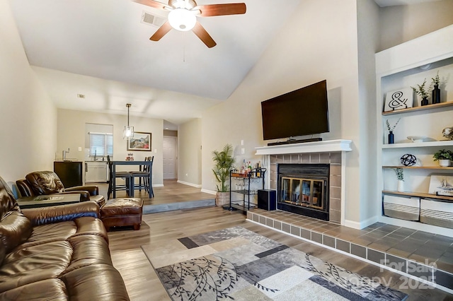 living room featuring built in features, wood finished floors, visible vents, baseboards, and a tile fireplace