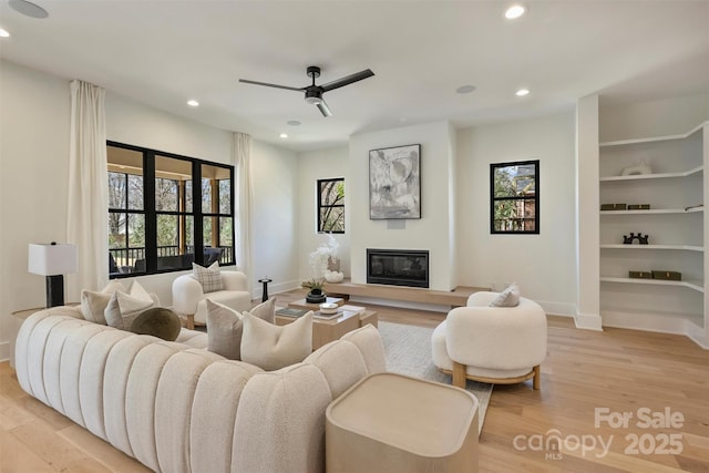 living room with baseboards, recessed lighting, a glass covered fireplace, and light wood-style floors