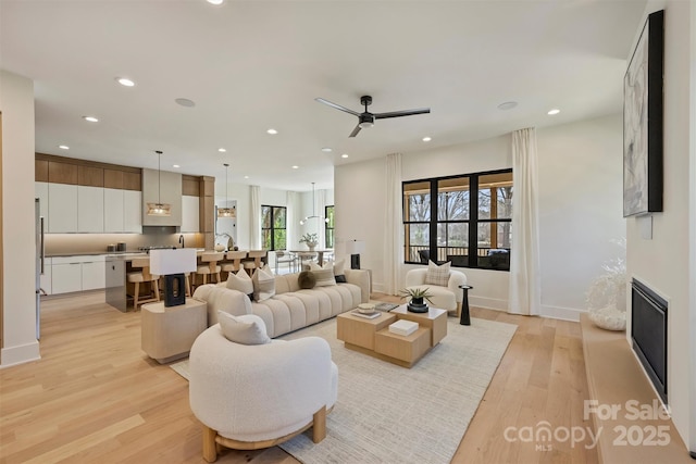 living room with recessed lighting, a ceiling fan, a glass covered fireplace, light wood-type flooring, and baseboards