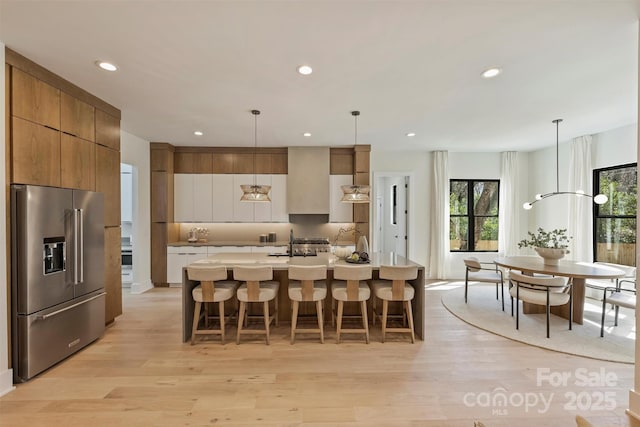 kitchen featuring high end refrigerator, a kitchen breakfast bar, light wood-style floors, brown cabinetry, and modern cabinets