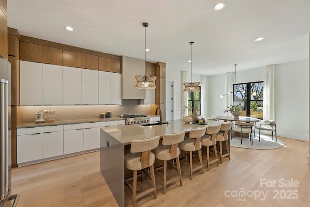 kitchen with white cabinets, an island with sink, stove, light wood-type flooring, and a sink