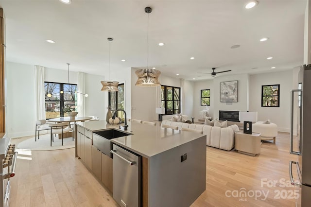 kitchen featuring a center island with sink, dishwasher, light wood-type flooring, a sink, and recessed lighting