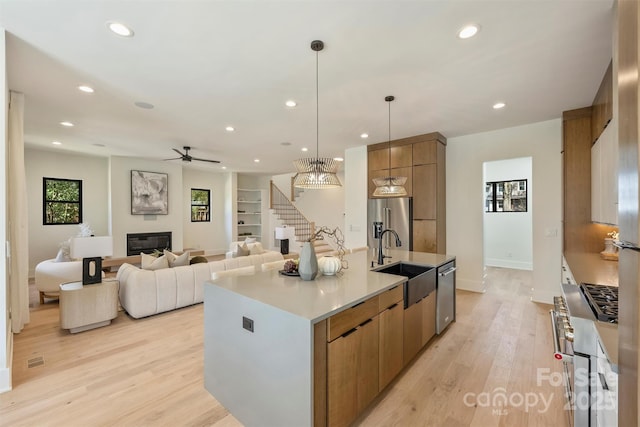 kitchen with brown cabinets, stainless steel appliances, a glass covered fireplace, a sink, and modern cabinets