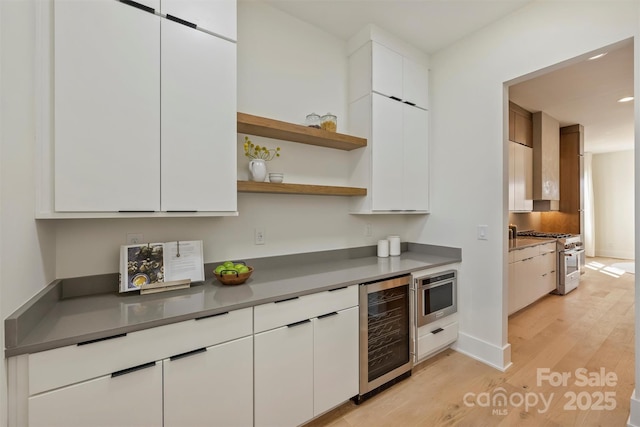 kitchen with high end stove, light wood-style flooring, beverage cooler, white cabinets, and open shelves