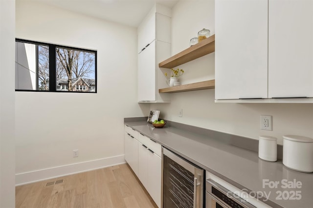 kitchen featuring light wood finished floors, beverage cooler, white cabinets, modern cabinets, and open shelves