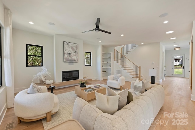 living room with recessed lighting, visible vents, stairway, a glass covered fireplace, and light wood-type flooring