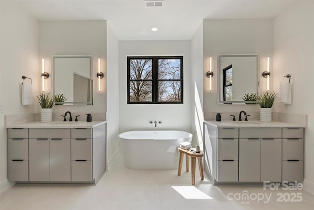 bathroom featuring two vanities, a sink, and a freestanding bath