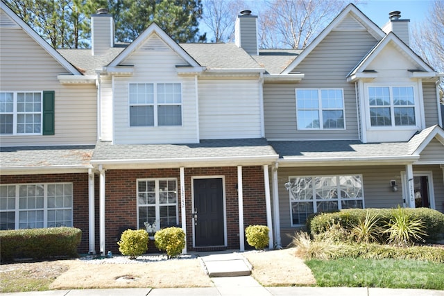 multi unit property with a shingled roof, brick siding, and a chimney