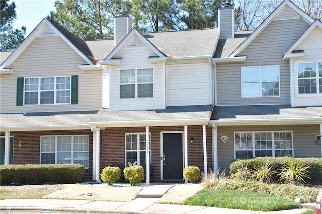 townhome / multi-family property with brick siding, a chimney, and a shingled roof