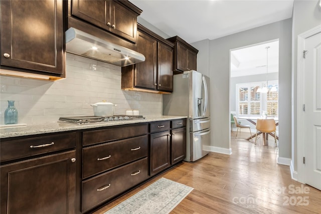 2934 Hiddenbrook Way, Fort Mill, SC 29707 - kitchen with stainless steel appliances, decorative backsplash, dark brown cabinets, exhaust hood, and light wood-type flooring
