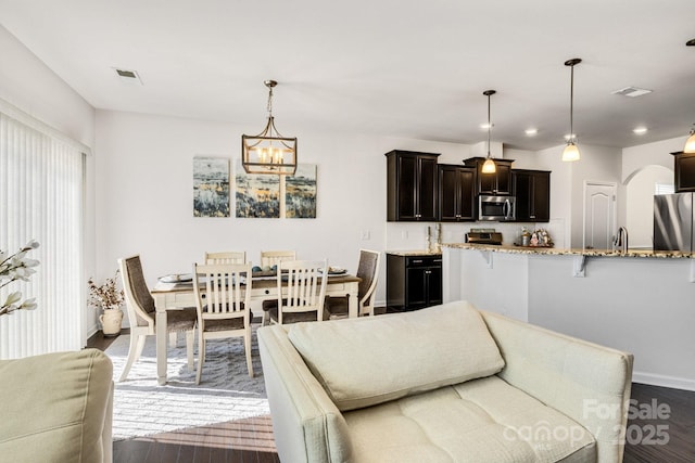 dining space featuring arched walkways, visible vents, dark wood finished floors, and an inviting chandelier