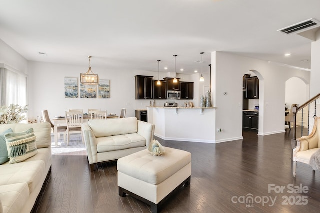 living room with arched walkways, visible vents, dark wood finished floors, and stairway