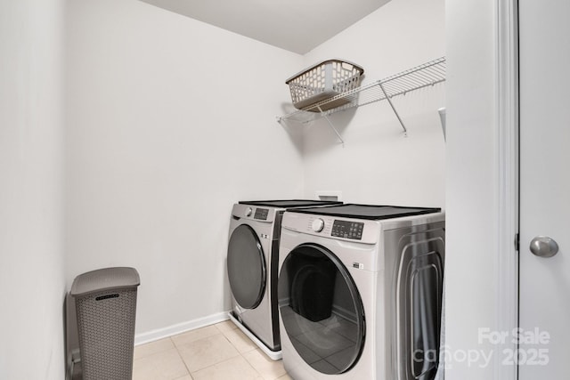 washroom featuring light tile patterned floors, laundry area, washing machine and clothes dryer, and baseboards