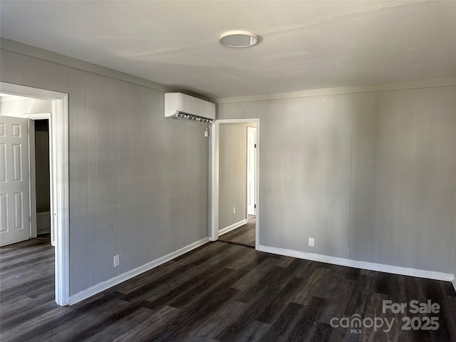 empty room with dark wood-style floors, a wall unit AC, and baseboards