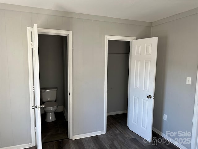 unfurnished bedroom with dark wood-style floors, a closet, a spacious closet, and baseboards