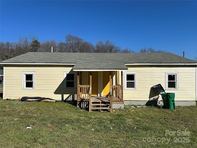 back of house with a porch, roof with shingles, and a yard