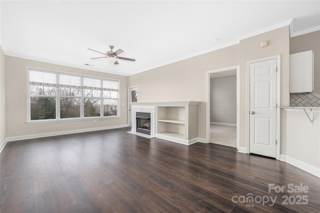 unfurnished living room featuring dark wood-style flooring, ornamental molding, a high end fireplace, ceiling fan, and baseboards