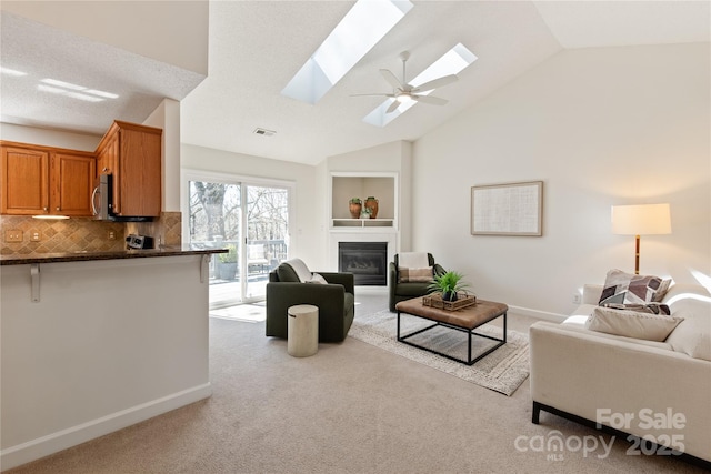 living room featuring carpet flooring, visible vents, baseboards, lofted ceiling with skylight, and a glass covered fireplace