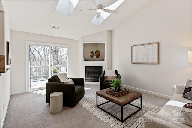 living area featuring visible vents, a glass covered fireplace, carpet flooring, vaulted ceiling with skylight, and baseboards