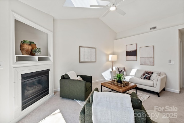 living room featuring carpet floors, visible vents, a ceiling fan, a glass covered fireplace, and vaulted ceiling with skylight