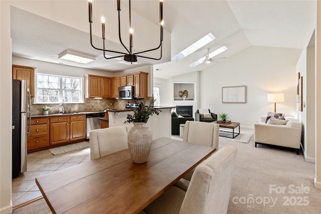 dining space with light tile patterned floors, light colored carpet, a glass covered fireplace, vaulted ceiling with skylight, and baseboards