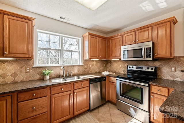 kitchen featuring light tile patterned floors, a sink, visible vents, appliances with stainless steel finishes, and brown cabinetry