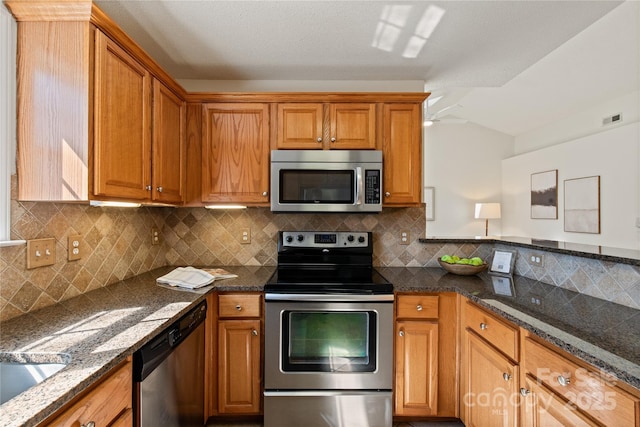 kitchen featuring appliances with stainless steel finishes, dark stone countertops, visible vents, and brown cabinets