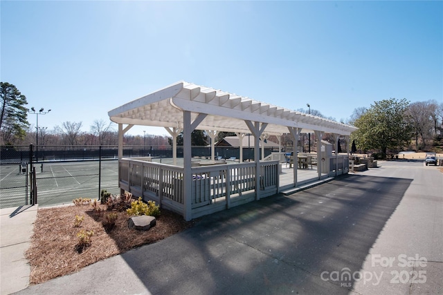 view of property's community featuring a tennis court, fence, and a pergola