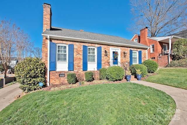 view of front facade featuring brick siding, a chimney, a front yard, and a shingled roof