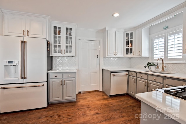 kitchen featuring dark wood-style flooring, gray cabinetry, white cabinets, a sink, and white appliances