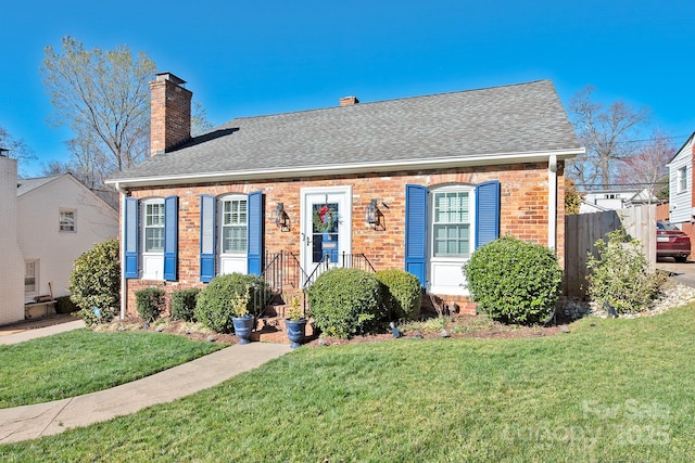 view of front of property with brick siding, a chimney, a front lawn, and roof with shingles