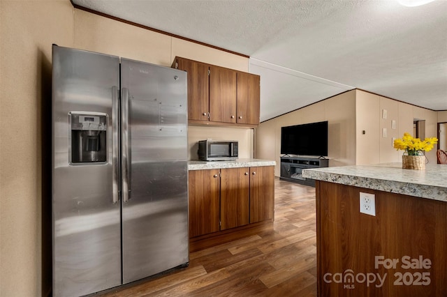 kitchen with a textured ceiling, appliances with stainless steel finishes, dark wood-style flooring, and brown cabinets