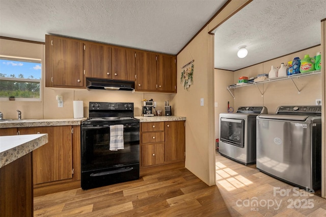 kitchen featuring washing machine and dryer, light wood-style flooring, under cabinet range hood, brown cabinets, and black electric range oven