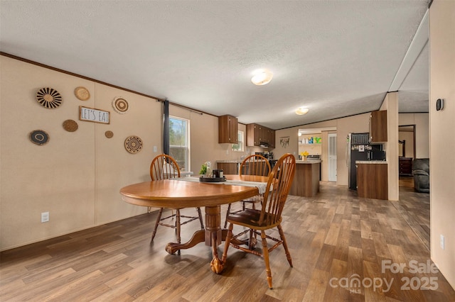 dining space with crown molding, a textured ceiling, vaulted ceiling, and wood finished floors